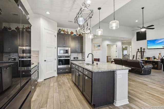 kitchen featuring pendant lighting, sink, dark brown cabinets, stainless steel appliances, and an island with sink