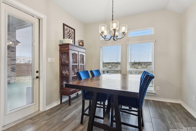 dining area with dark wood-type flooring, a chandelier, and vaulted ceiling