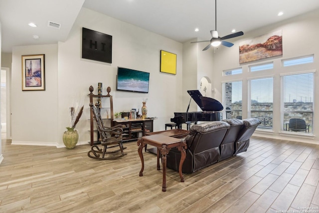 living room featuring ceiling fan, light hardwood / wood-style floors, and a high ceiling