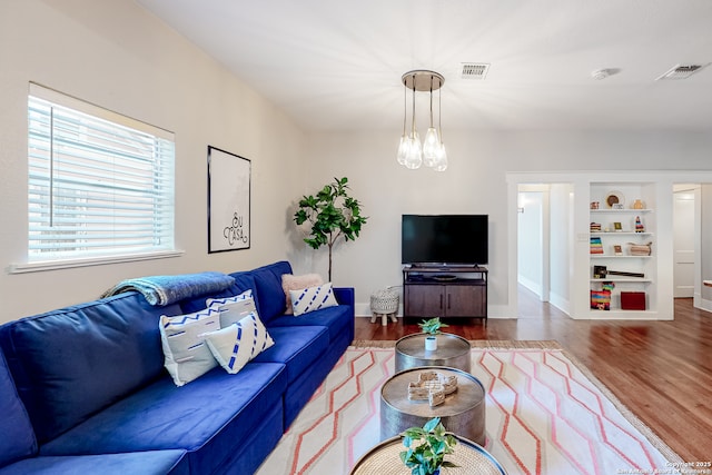 living room featuring hardwood / wood-style flooring, built in features, and a chandelier