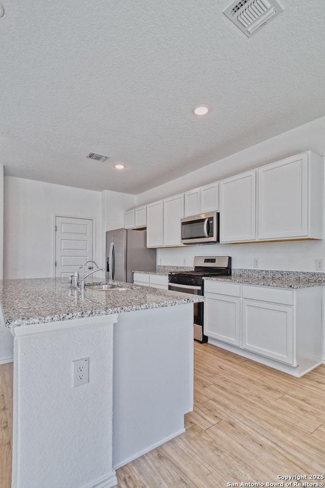 kitchen featuring sink, appliances with stainless steel finishes, white cabinetry, an island with sink, and light wood-type flooring