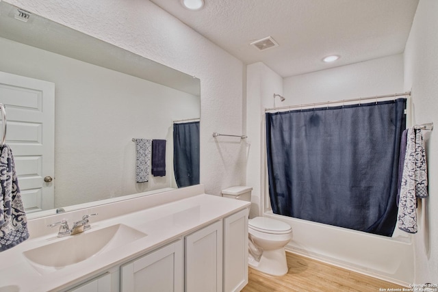 full bathroom with shower / bathtub combination with curtain, hardwood / wood-style flooring, vanity, a textured ceiling, and toilet