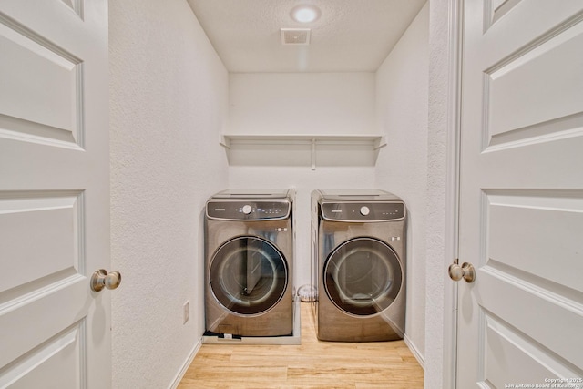 laundry area with light wood-type flooring, a textured ceiling, and washer and clothes dryer