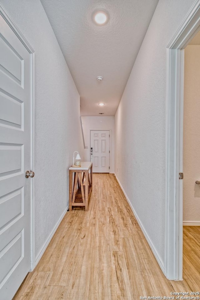 corridor with a textured ceiling and light hardwood / wood-style floors