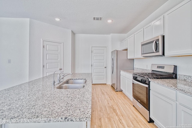 kitchen with appliances with stainless steel finishes, white cabinetry, sink, light stone counters, and light hardwood / wood-style flooring