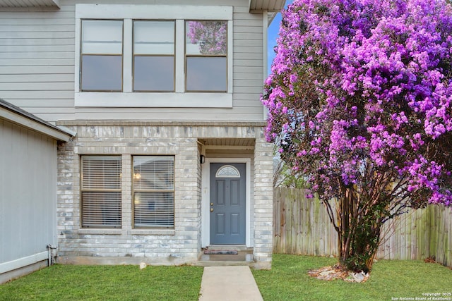 doorway to property featuring stone siding, a lawn, and fence