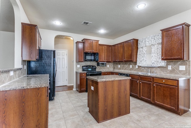 kitchen featuring sink, tasteful backsplash, light stone counters, black appliances, and a kitchen island