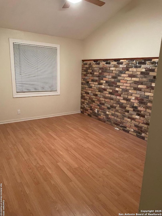 empty room with ceiling fan, brick wall, vaulted ceiling, and light hardwood / wood-style flooring