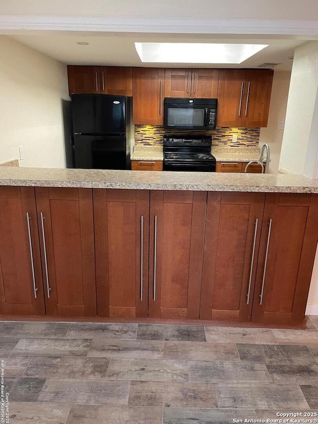 kitchen featuring sink, hardwood / wood-style floors, light stone counters, black appliances, and kitchen peninsula