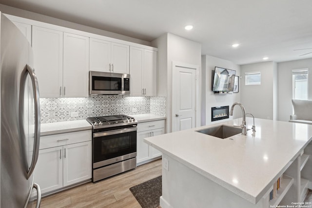 kitchen featuring sink, appliances with stainless steel finishes, an island with sink, white cabinets, and light wood-type flooring