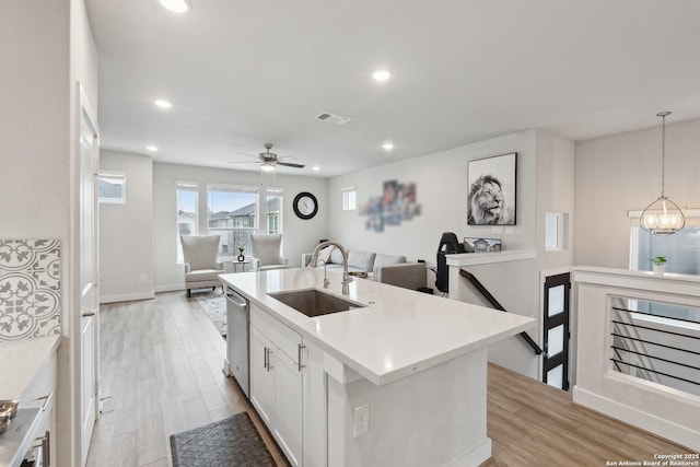 kitchen with sink, stainless steel dishwasher, pendant lighting, a kitchen island with sink, and white cabinets