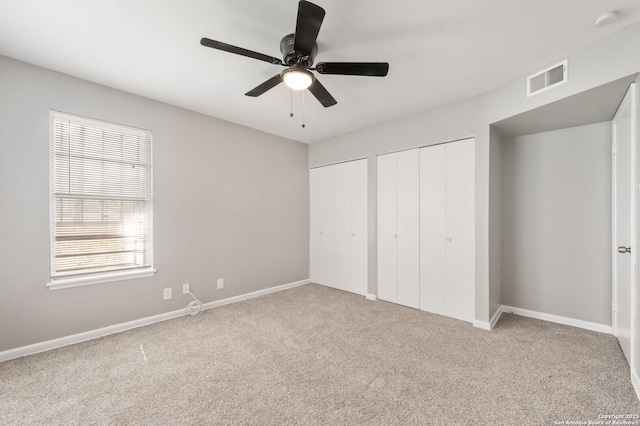 unfurnished bedroom with multiple closets, light colored carpet, and ceiling fan