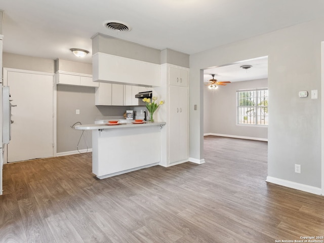 kitchen with a breakfast bar area, light wood-type flooring, kitchen peninsula, ceiling fan, and white cabinets