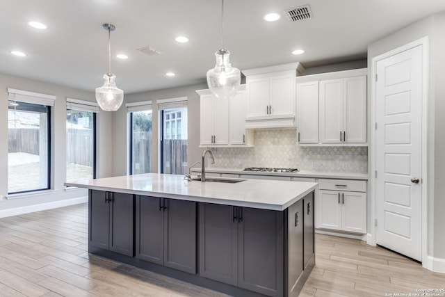 kitchen featuring white cabinetry, an island with sink, sink, and pendant lighting