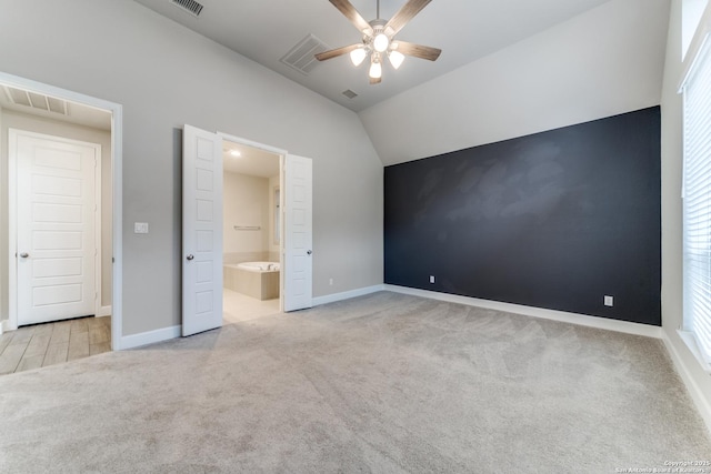 unfurnished bedroom featuring ceiling fan, light colored carpet, lofted ceiling, and ensuite bath