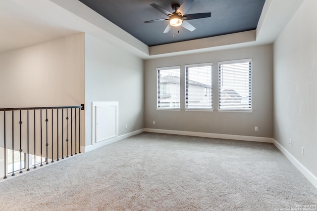 carpeted spare room with a raised ceiling and ceiling fan