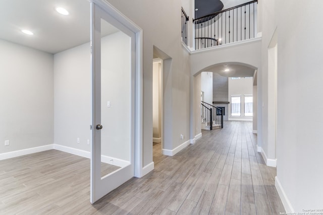 hall with a high ceiling and light hardwood / wood-style floors