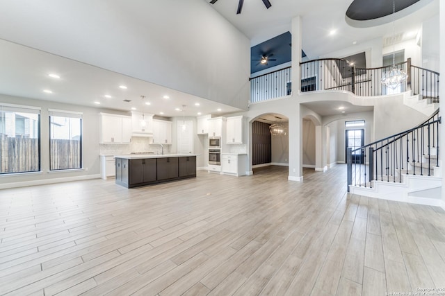 unfurnished living room with ceiling fan with notable chandelier, a healthy amount of sunlight, sink, and light hardwood / wood-style floors