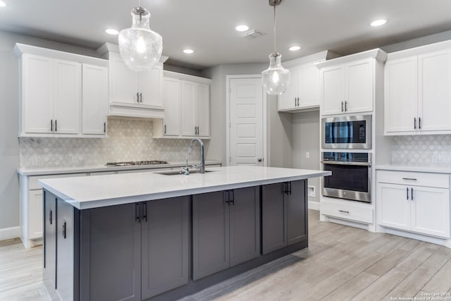 kitchen featuring appliances with stainless steel finishes, a kitchen island with sink, pendant lighting, and white cabinets