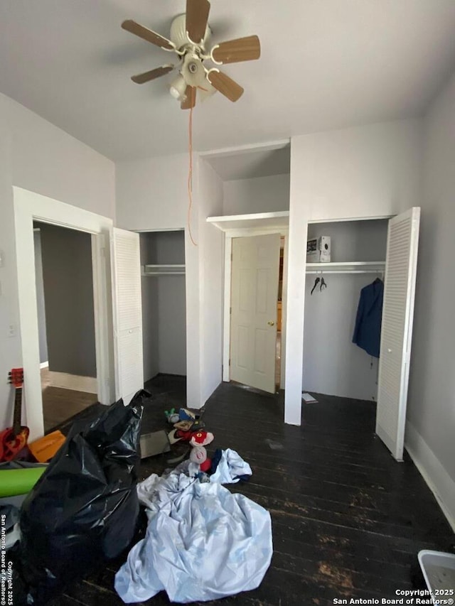 bedroom with two closets, dark hardwood / wood-style floors, and ceiling fan