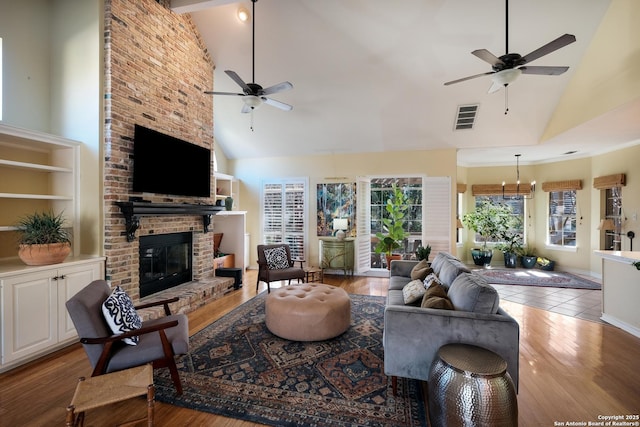 living room with high vaulted ceiling, ceiling fan with notable chandelier, a fireplace, and light hardwood / wood-style floors