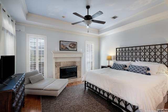 bedroom featuring a tiled fireplace, hardwood / wood-style flooring, ornamental molding, and a raised ceiling