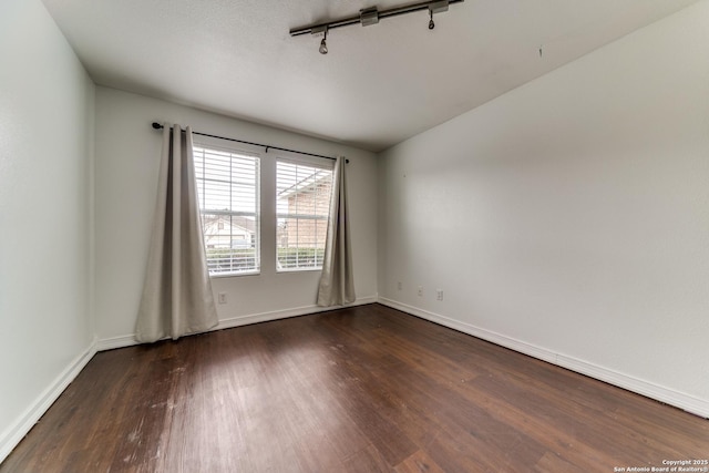 spare room featuring dark hardwood / wood-style flooring and track lighting