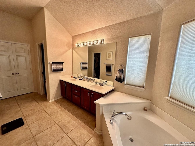 bathroom featuring vanity, a textured ceiling, vaulted ceiling, tile patterned floors, and a tub