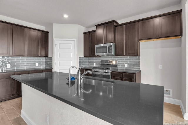 kitchen with sink, dark brown cabinets, stainless steel appliances, and a center island with sink