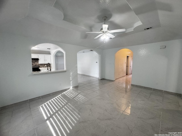 empty room with sink, ceiling fan, and a tray ceiling