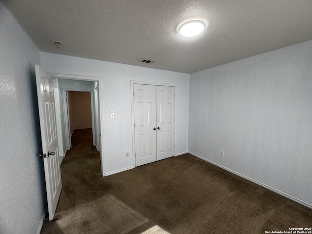 unfurnished bedroom featuring a closet, a textured ceiling, and dark colored carpet