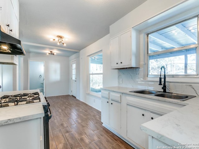 kitchen featuring black gas range oven, sink, backsplash, wood-type flooring, and white cabinets