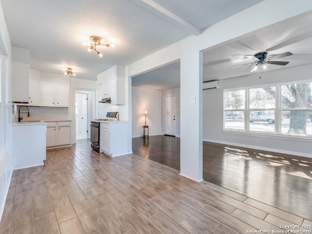 kitchen with sink, white cabinetry, a wall mounted air conditioner, light hardwood / wood-style floors, and gas range oven