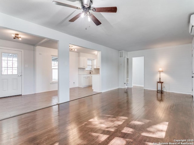 unfurnished living room with sink, a wall mounted air conditioner, dark wood-type flooring, and ceiling fan