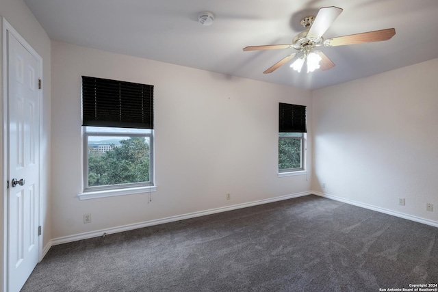 spare room with ceiling fan, a healthy amount of sunlight, and dark carpet