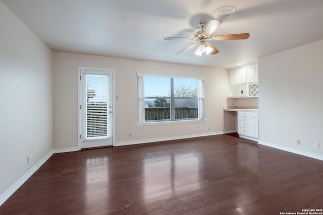 unfurnished living room featuring ceiling fan, dark hardwood / wood-style floors, and built in desk