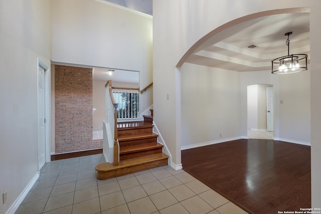 staircase featuring tile patterned flooring, a raised ceiling, an inviting chandelier, and a high ceiling