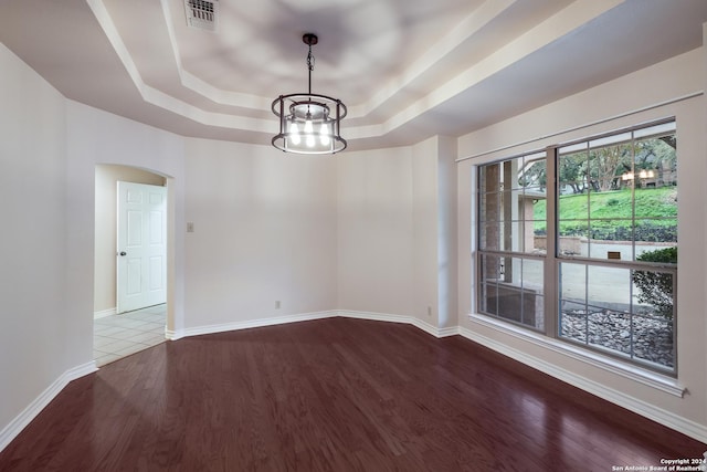 unfurnished room with a raised ceiling, hardwood / wood-style floors, and a notable chandelier