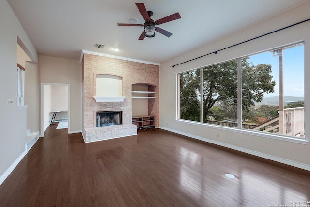 unfurnished living room featuring dark hardwood / wood-style flooring, a brick fireplace, built in shelves, and ceiling fan