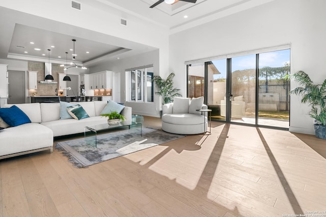 living room featuring a towering ceiling, light hardwood / wood-style flooring, ceiling fan, and a tray ceiling