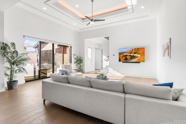 living room featuring a raised ceiling, hardwood / wood-style flooring, ceiling fan, and a towering ceiling