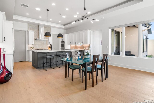 dining space featuring sink, a tray ceiling, and light hardwood / wood-style flooring