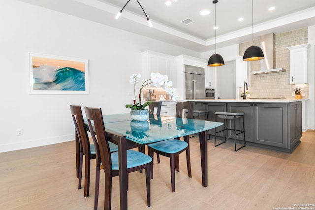 dining space with sink, a raised ceiling, and light hardwood / wood-style floors