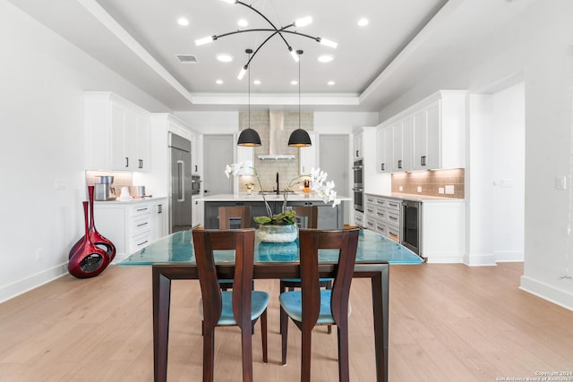 dining space featuring wine cooler, sink, light wood-type flooring, a tray ceiling, and a notable chandelier