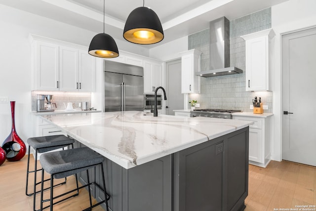 kitchen featuring wall chimney range hood, a large island with sink, white cabinets, and appliances with stainless steel finishes