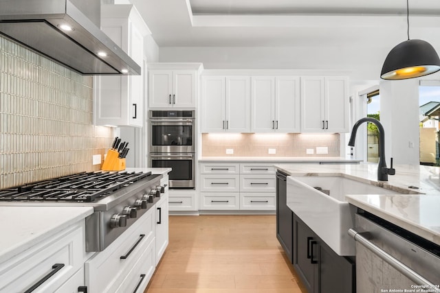 kitchen featuring wall chimney exhaust hood, white cabinetry, tasteful backsplash, decorative light fixtures, and appliances with stainless steel finishes