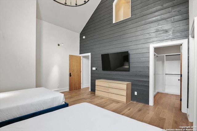 bedroom with hardwood / wood-style flooring, a walk in closet, high vaulted ceiling, and wood walls