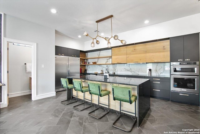 kitchen with a kitchen bar, hanging light fixtures, an island with sink, stainless steel appliances, and backsplash