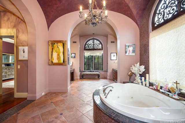 bathroom featuring tiled tub, vaulted ceiling, a notable chandelier, and vanity