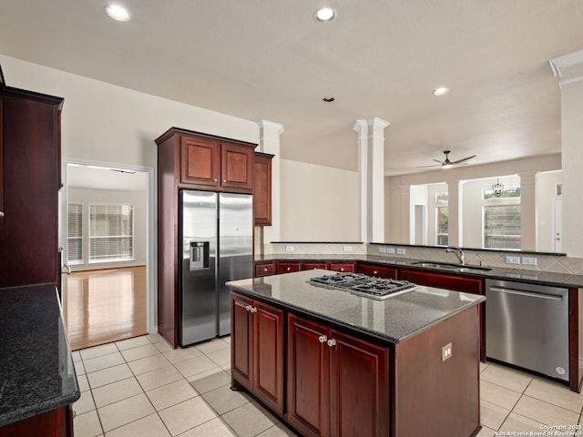 kitchen featuring sink, appliances with stainless steel finishes, dark stone countertops, decorative columns, and a center island